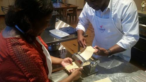 A man and woman are using a pasta machine to roll out dough in a kitchen setting.
