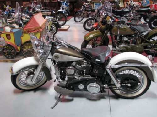 A vintage motorcycle with a chrome and white design, surrounded by various other classic bikes in a museum setting.