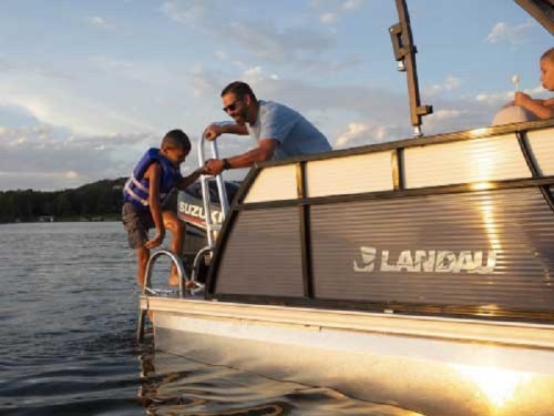 A man helps a boy climb onto a boat at sunset, with another child sitting on the boat. Water and trees are in the background.
