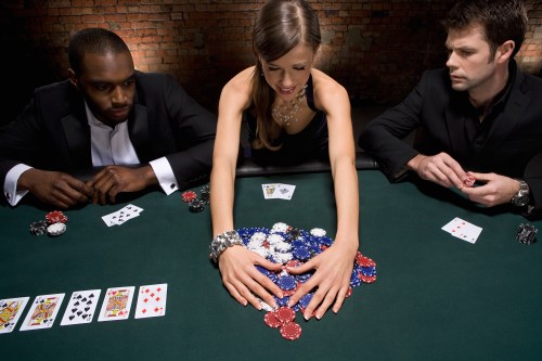 A woman in a black dress places chips on a poker table, flanked by two men in suits, with playing cards visible.
