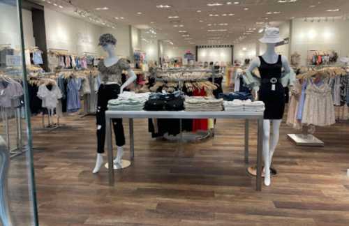 A clothing store interior featuring mannequins displaying outfits and racks of apparel in a bright, spacious setting.