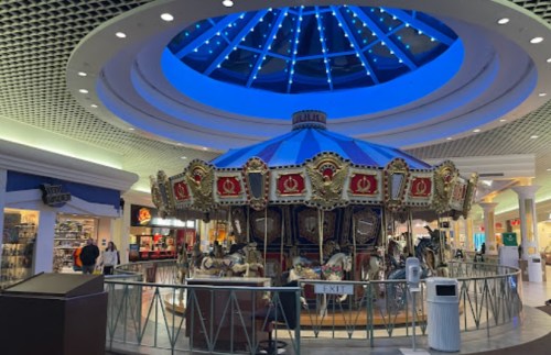 A colorful carousel with ornate decorations under a blue-lit ceiling in a shopping mall.