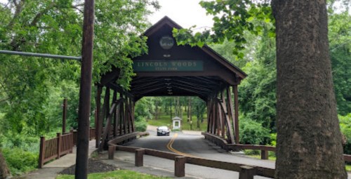 A covered bridge named Lincoln Woods, surrounded by lush greenery and a winding road leading through it.