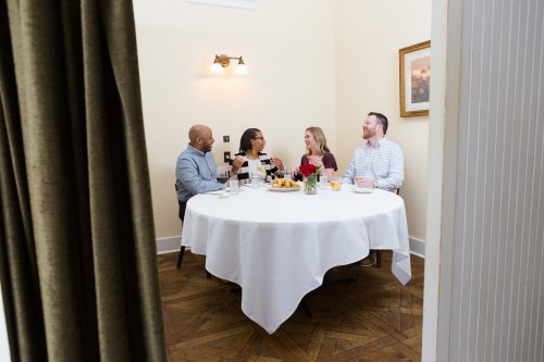 A group of four friends enjoying a meal together at a round table in a cozy restaurant setting.