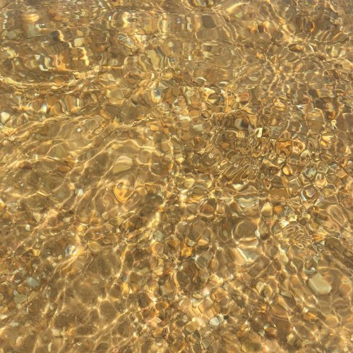 Clear water with rippling reflections, revealing smooth pebbles beneath the surface.