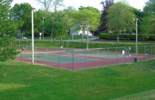 A view of empty tennis courts surrounded by greenery on a sunny day.