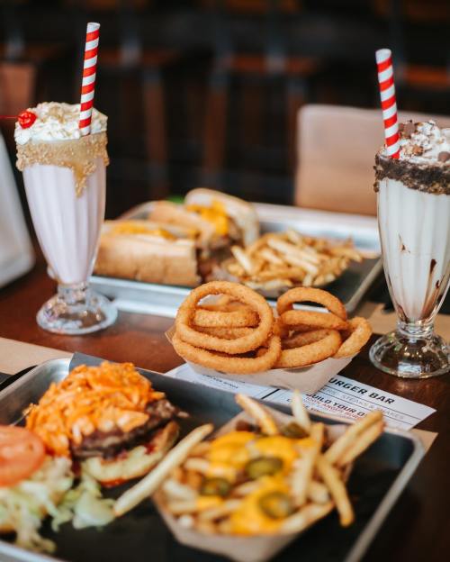 A table with burgers, onion rings, fries, and milkshakes topped with whipped cream and cherries.