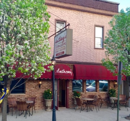Exterior of Anthony's restaurant with a brick facade, green trees, and outdoor seating under a red awning.