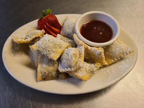 A plate of powdered sugar-dusted pastries with a side of dipping sauce and a strawberry garnish.
