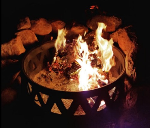 A glowing fire in a circular fire pit surrounded by rocks, illuminating the dark night.