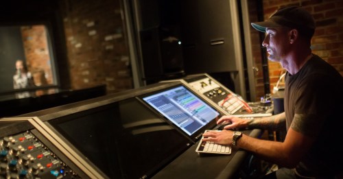 A sound engineer adjusts audio settings at a mixing console in a recording studio.