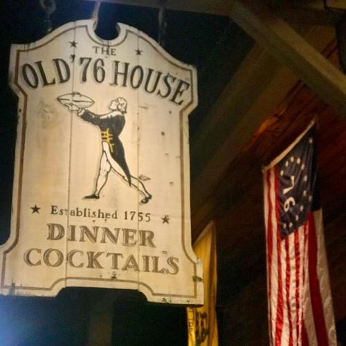 Sign for "The Old '76 House," established 1755, featuring dinner and cocktails, with a historical flag in the background.