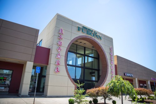 Exterior of a modern building with large windows and signage for "Fubonn" in a shopping plaza, surrounded by greenery.