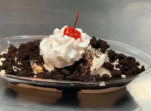 A dessert dish with layers of ice cream, chocolate sauce, crushed cookies, whipped cream, and a cherry on top.
