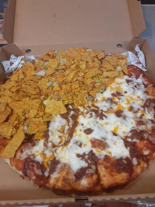 A pizza topped with melted cheese, sauce, and a layer of crunchy tortilla chips in a pizza box.