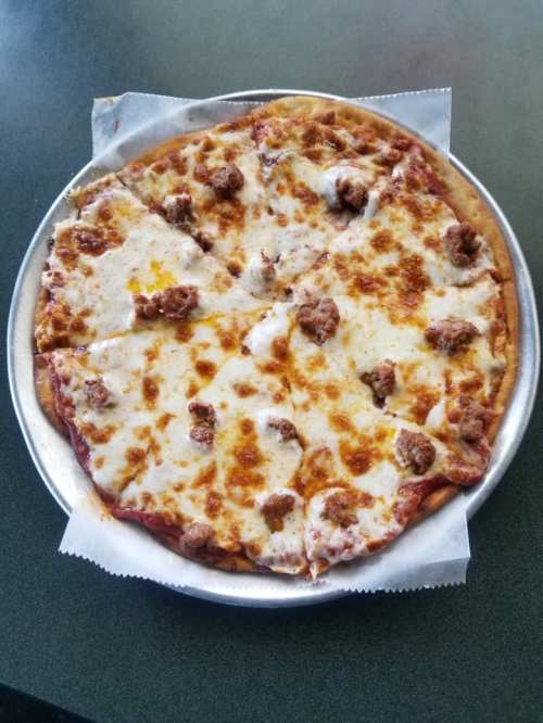 A round pizza with melted cheese and sausage toppings, sliced into eight pieces on a silver tray.