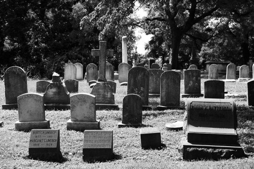 A black and white image of a cemetery with various gravestones and a peaceful, grassy landscape.