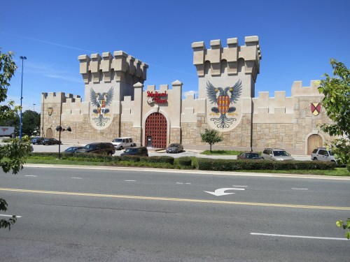 A large castle-themed building with towers and murals, set against a clear blue sky, viewed from the street.