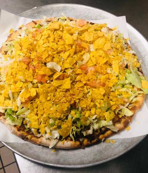 A pizza topped with lettuce, tomatoes, and crushed tortilla chips on a silver serving tray.