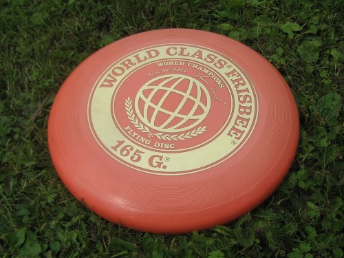 A red frisbee with "World Class Frisbee" and a globe design, resting on green grass.