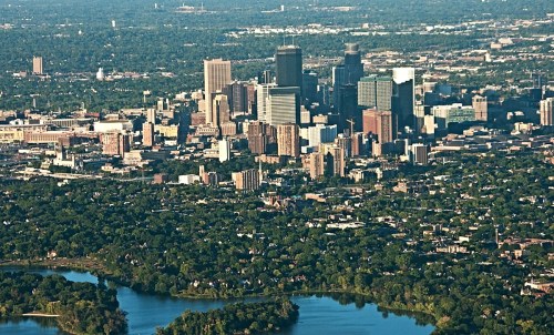 Aerial view of a city skyline surrounded by greenery and a river, showcasing tall buildings and urban landscape.