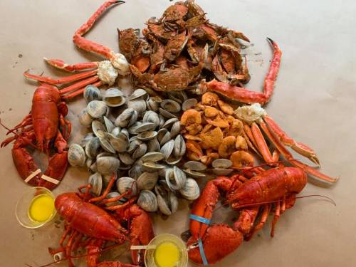 A seafood feast featuring lobsters, crabs, clams, and dipping sauces arranged on brown paper.
