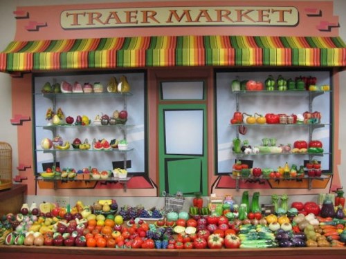 Colorful display of fruits and vegetables in a market setting, with shelves and a striped awning.