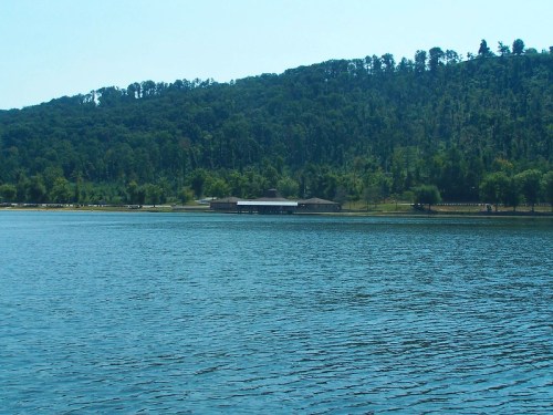 A serene lake scene with a distant shoreline, green hills, and a small building near the water's edge.