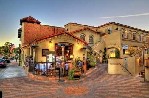 Charming café with outdoor seating, surrounded by colorful planters and a scenic walkway, under a clear sky.