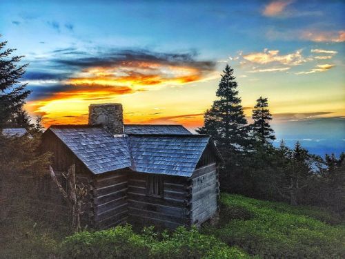 A rustic cabin surrounded by trees at sunset, with vibrant orange and blue skies in the background.