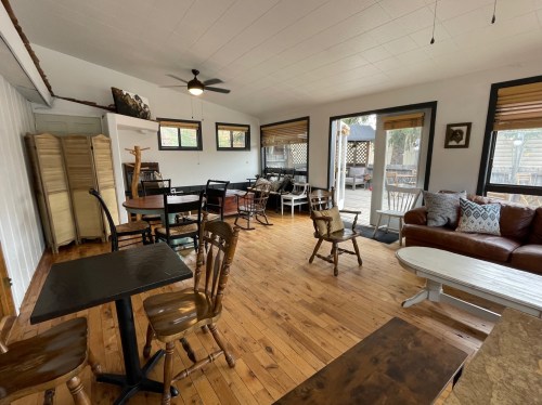 Cozy interior space with wooden floors, tables, chairs, and large windows letting in natural light.
