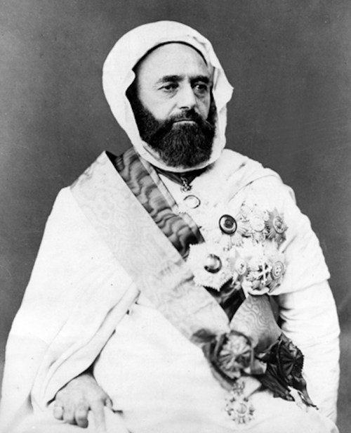 A historical portrait of a man in traditional attire, adorned with medals and a sash, seated and looking thoughtfully.