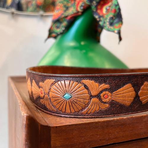A decorative leather belt featuring fish motifs and colorful inlays, displayed against a vibrant background.
