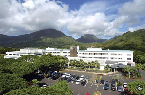 Aerial view of a modern building surrounded by trees and mountains under a partly cloudy sky.