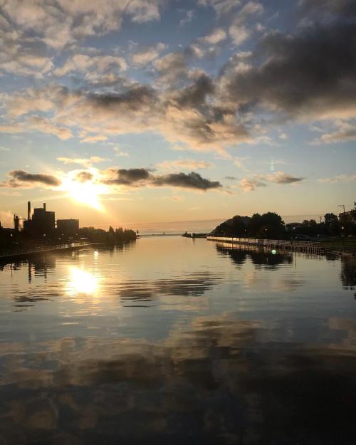 Sunset over a calm waterway, with reflections of clouds and buildings, creating a serene and picturesque scene.