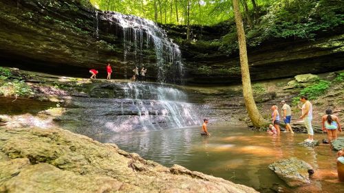 A scenic waterfall surrounded by lush greenery, with people enjoying the water and exploring the area.