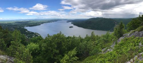 A panoramic view of a river surrounded by lush greenery and distant hills under a partly cloudy sky.