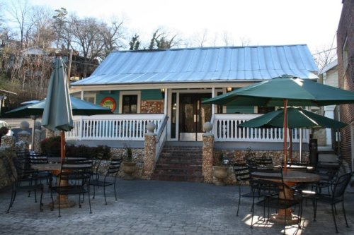 A charming building with a metal roof, surrounded by outdoor seating and green umbrellas on a sunny day.