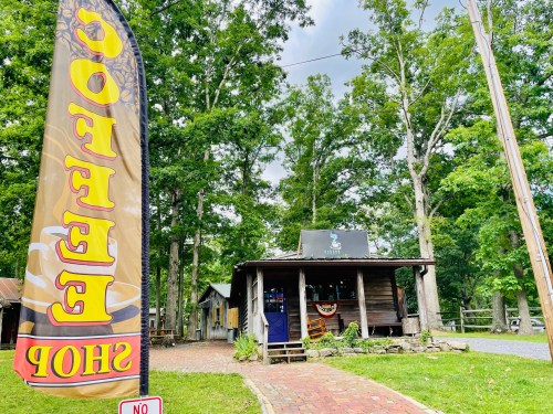 A cozy coffee shop nestled among trees, featuring a colorful sign and rustic wooden exterior.