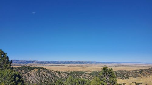 A vast landscape with rolling hills and a clear blue sky, dotted with sparse trees and open fields.
