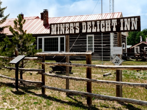 Sign for Miner's Delight Inn in front of a rustic building with a wooden fence and grassy area.