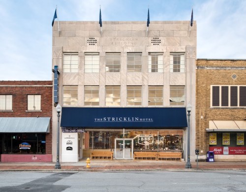 Historic Stricklin Hotel building with a modern entrance, flanked by brick storefronts on a city street.