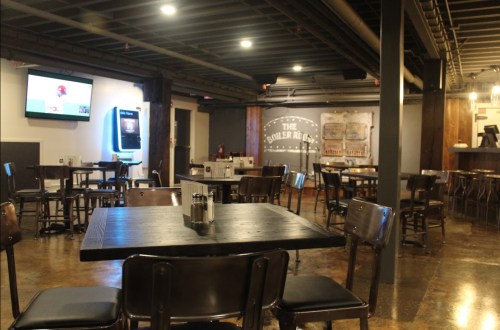 Interior of a casual dining space with wooden tables, chairs, and a TV on the wall. The atmosphere is relaxed and inviting.