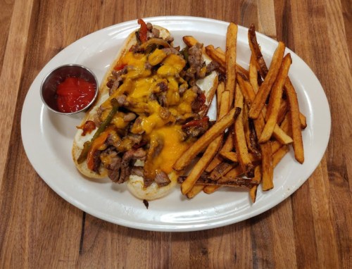 A plate featuring a loaded cheesesteak with peppers and onions, served with crispy fries and a side of ketchup.