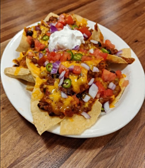 A plate of nachos topped with cheese, ground beef, tomatoes, onions, jalapeños, and a dollop of sour cream.