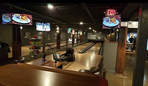 A bowling alley with two screens, a snack bar, and a bowling lane, featuring a "Turkey Season" sign on the wall.