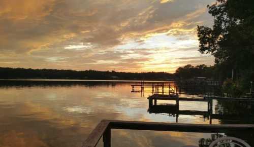 A serene lake at sunset, with colorful clouds reflecting on the water and wooden docks lining the shore.