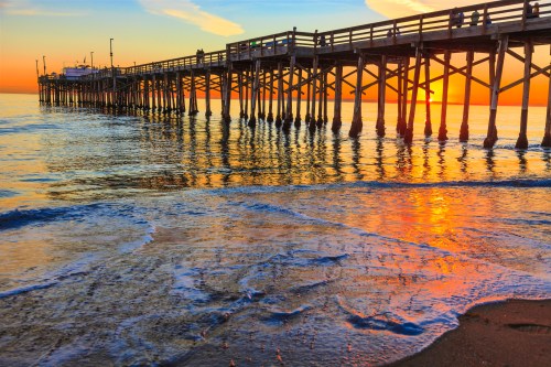 A sunset view of a pier extending over calm waters, reflecting vibrant orange and blue hues.