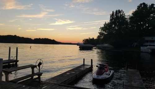 A serene lake at sunset, with a jet ski docked and silhouettes of trees in the background.