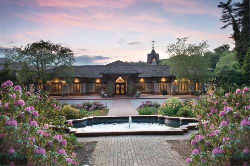 A scenic view of a building with a fountain and blooming flowers at sunset, surrounded by trees and a peaceful atmosphere.